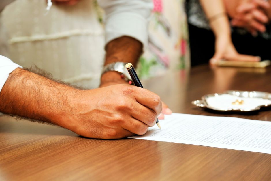 A close-up view of a person's hands in business attire signing an official document with a fountain pen, symbolizing the legal requirements of real estate licensing.