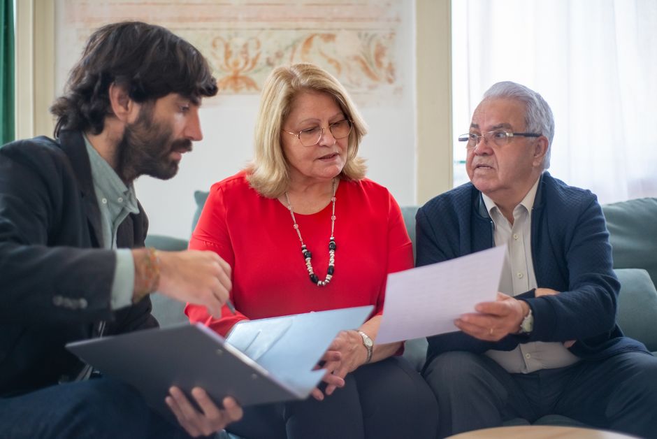 A couple sits at a clean, well-lit desk with an advisor who is pointing to a detail on a contract, symbolizing the legal and financial process of buying a home.
