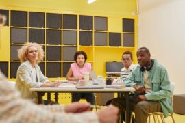 Diverse group of professionals sit around a modern conference table, collaborating and reviewing documents, representing a...