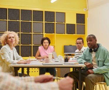 Diverse group of professionals sit around a modern conference table, collaborating and reviewing documents, representing a...