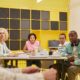 Diverse group of professionals sit around a modern conference table, collaborating and reviewing documents, representing a...