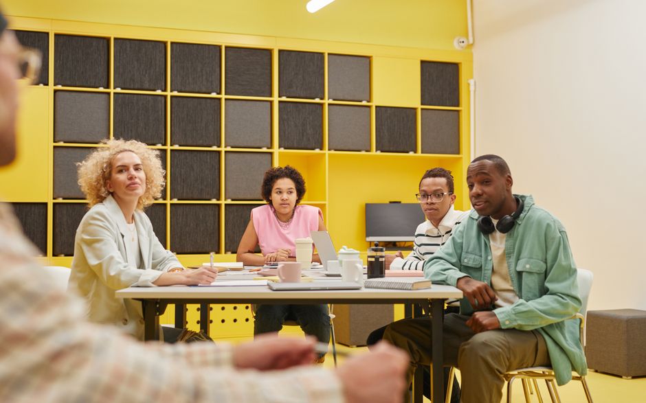 Diverse group of professionals sit around a modern conference table, collaborating and reviewing documents, representing a...