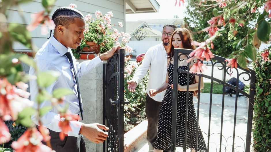 A friendly real estate agent stands with a young couple in front of a beautiful modern home, showcasing the property.