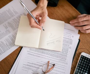 Person sits at a clean, modern desk, carefully reviewing a real estate contract with a pen and calculator, symbolizing fin...