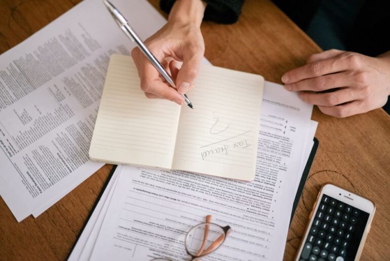Person sits at a clean, modern desk, carefully reviewing a real estate contract with a pen and calculator, symbolizing fin...